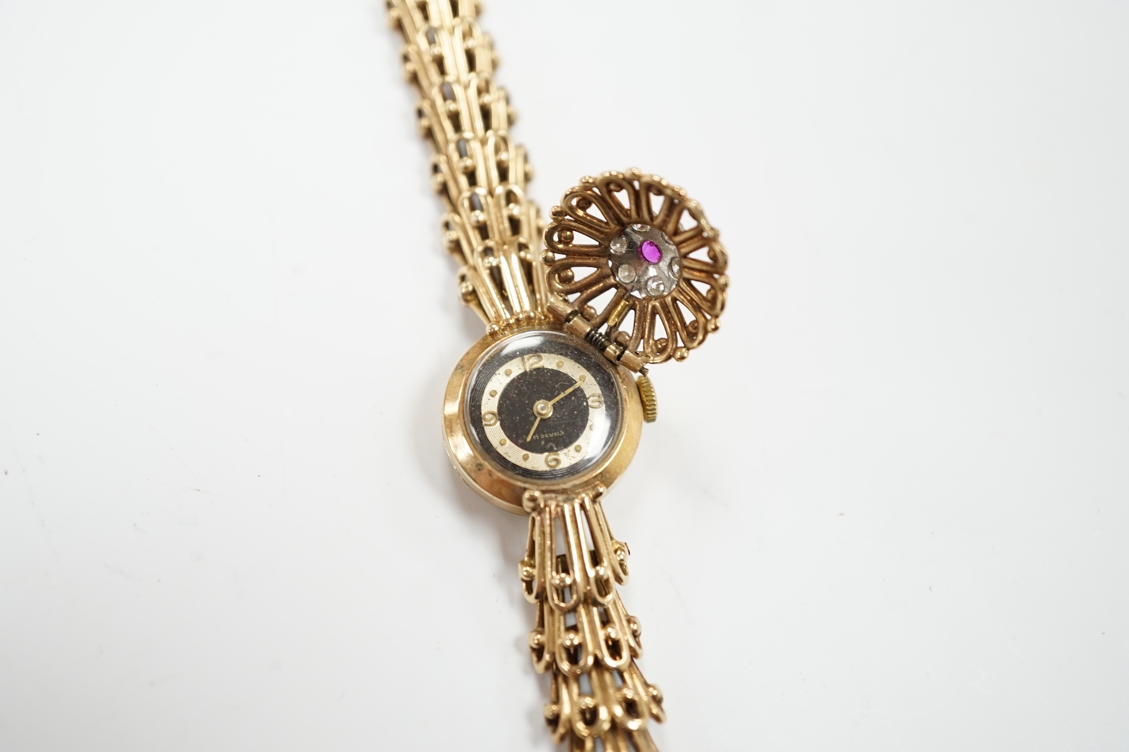A lady's yellow metal manual wind bracelet watch, the dial with ruby and diamond cluster set hinged cover, overall length 16.3cm